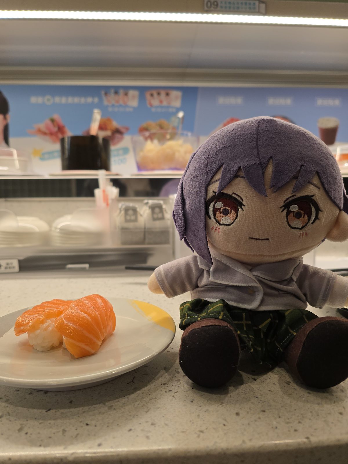 回転寿司のカウンターでぬいぐるみと寿司皿を撮った写真。飲食店でのぬい撮り例